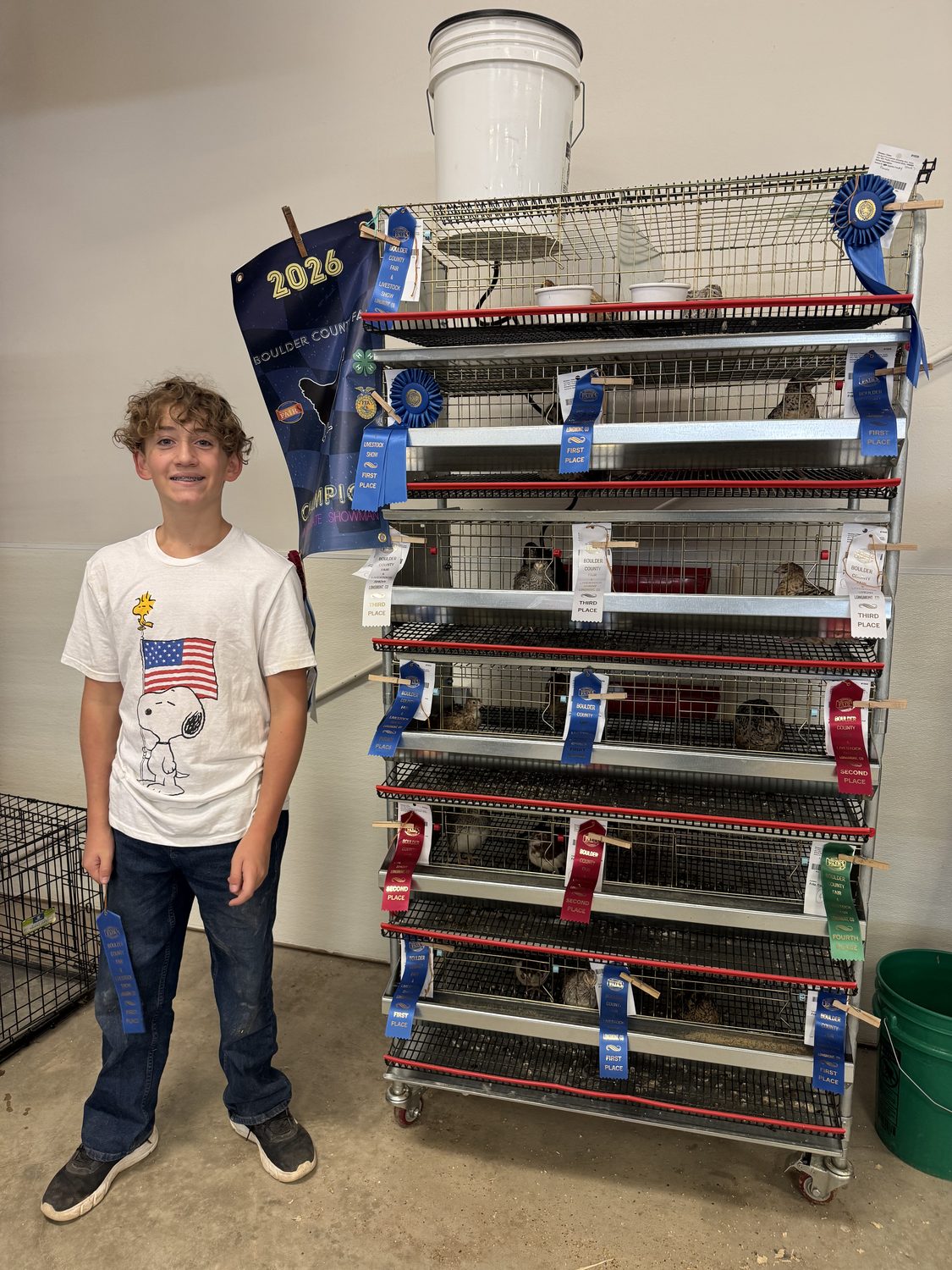 Colin standing beside the quail cage rack at the Boulder County Fair 2026, hung with ribbons